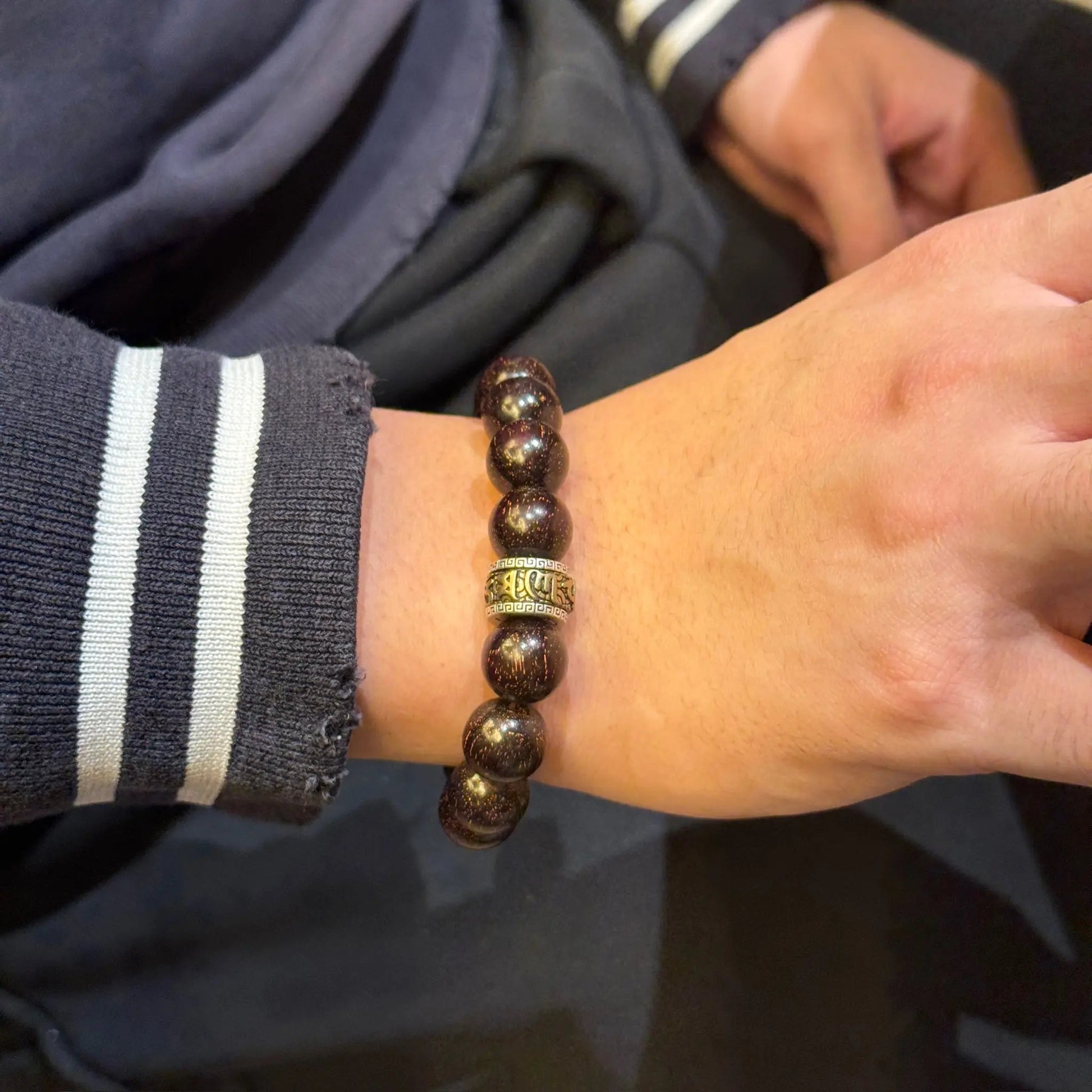 Men's sandalwood bracelet with obsidian charm featuring a golden pixiu charm on a hand.